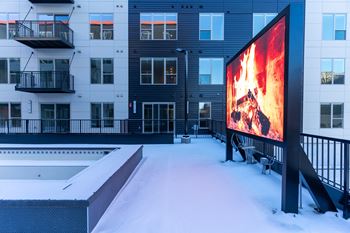 A large screen is lit up with a fire scene in front of a snowy building.